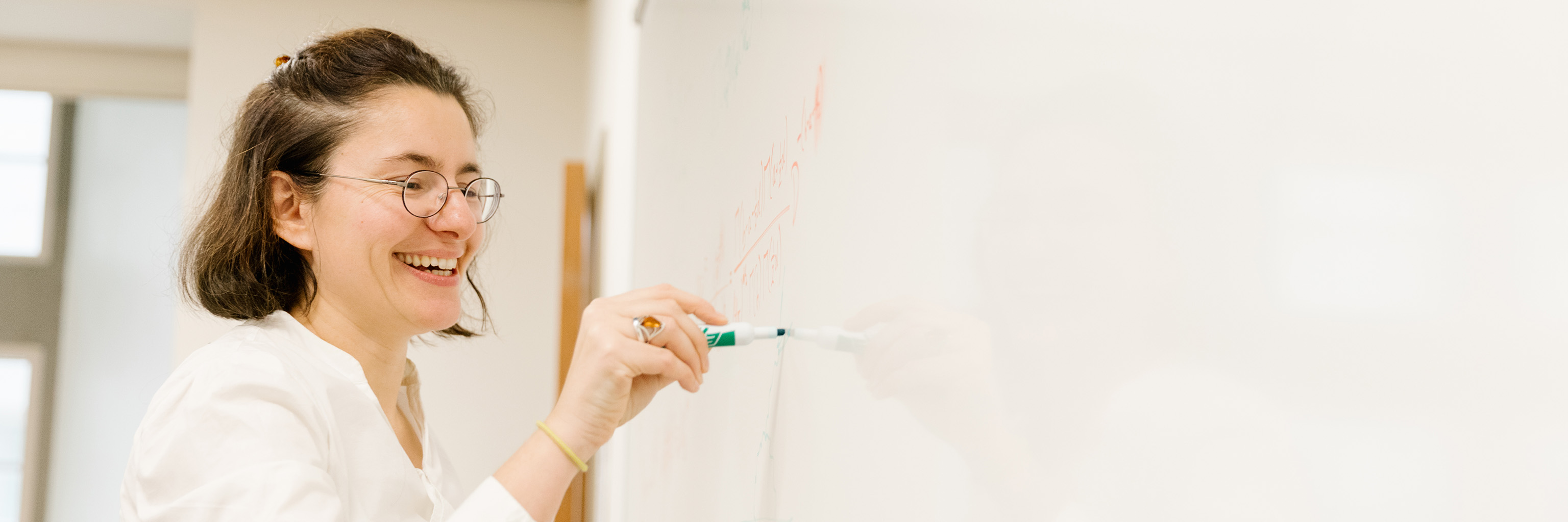 Close up of a woman smiling as she writes on a white board