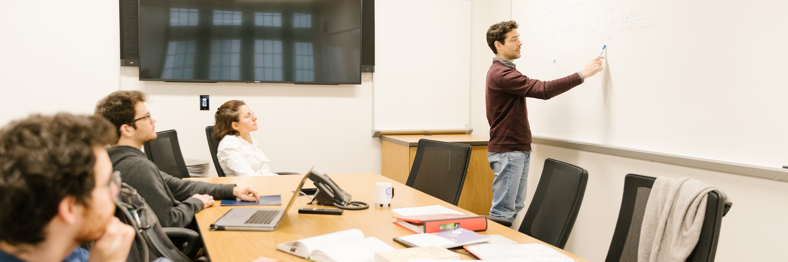 Graduate student gesturing to a white board as he leads a small group discussion