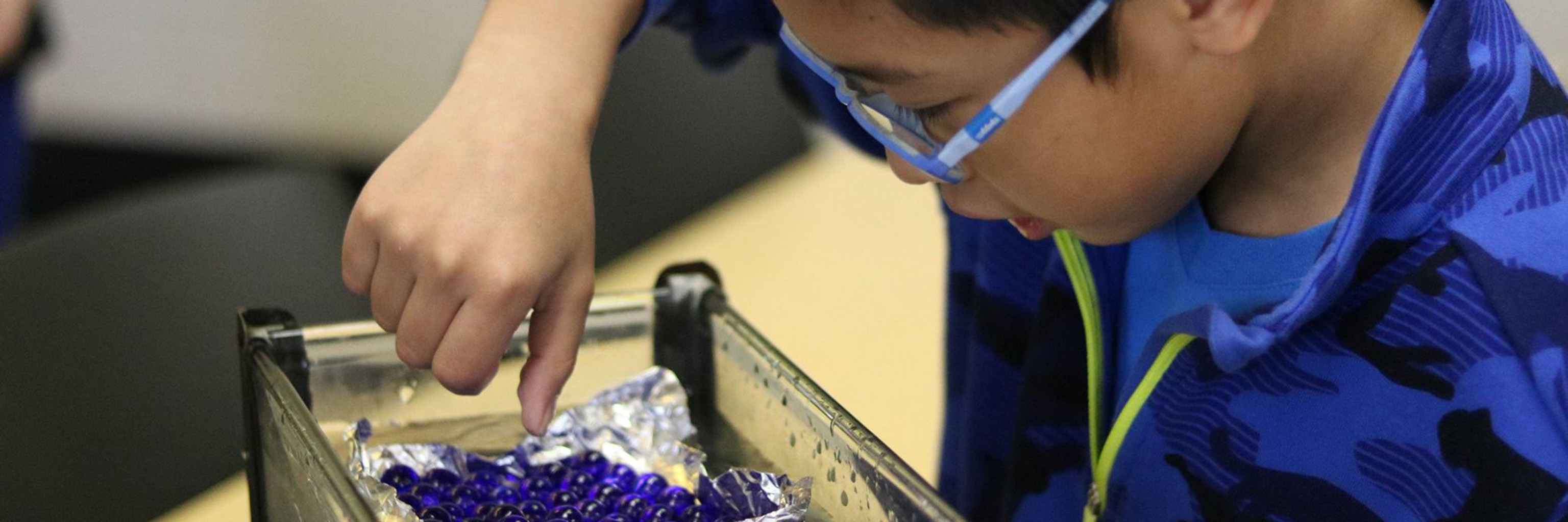 Young boy hovering over a science experiment using a tub of marbles 