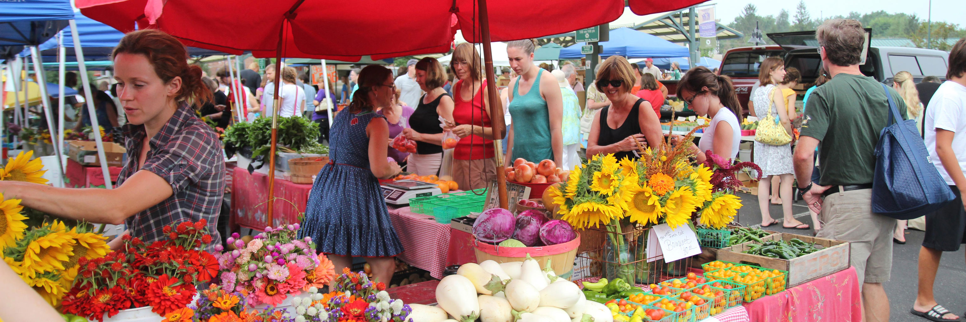 Crowd shopping for flowers and produce outdoors at the Bloomington Farmers Market. 