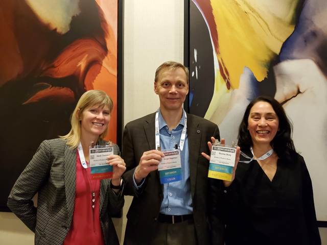 Three people smiling and displaying passes for the APS convocation
