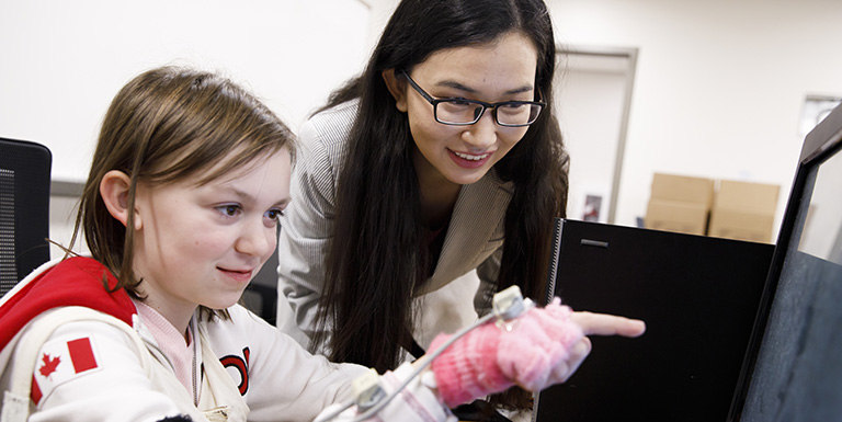 A woman working with a young girl at a computer station.