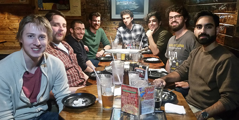 Graduate students smiling for the camera as they sit around a table for a meal.