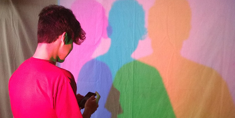 A man looking at his shadow, which has been split into pink, blue, and yellow overlapping shadows.