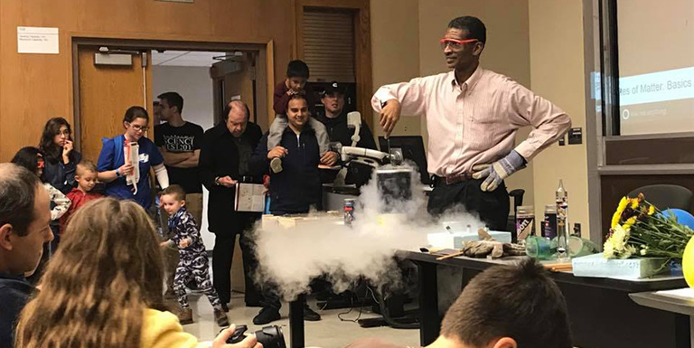A professor performing a physics demonstration with dry ice for a group of school-age children.