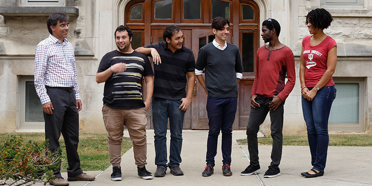 Five students and a professor laughing and talking to one another outside of a classroom building.
