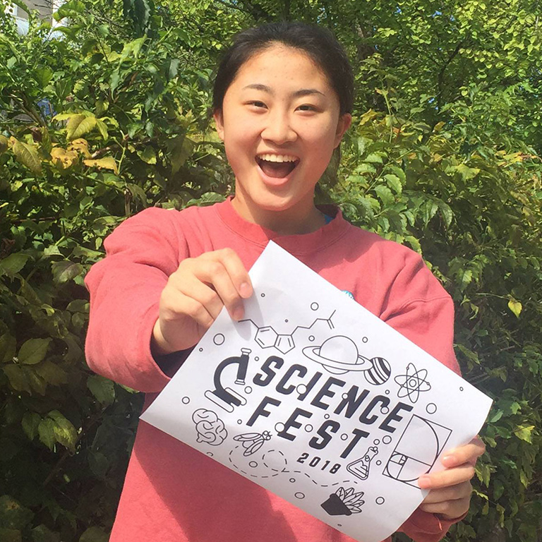 A woman smiling and holding a "Science Fest 2018" sign.